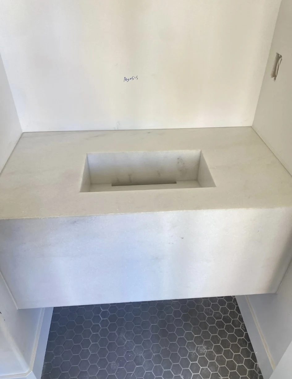 Peoria bathroom with a custom pale stone sink, integrated rectangular basin, and deep stone front apron above dark hexagonal floor tiles