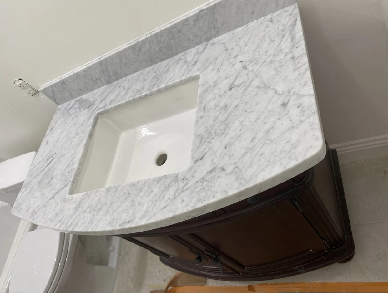 Scottsdale bathroom vanity with a curved veined stone countertop, matching backsplash, and white undermount sink above dark wood cabinetry